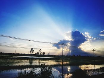 Silhouette electricity pylon by lake against sky during sunset