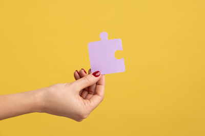 Cropped hands of woman using mobile phone against yellow background
