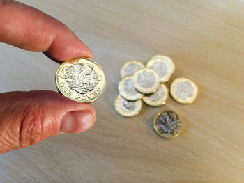 Cropped hand of person holding one pound coin over table