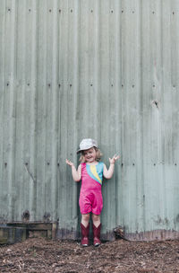 A young girl stands near a barn wearing a leotard and cowgirl boots.