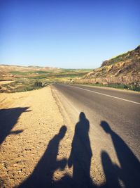 Shadow of people on road against clear blue sky