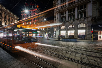 Illuminated railroad tracks amidst buildings in city at night