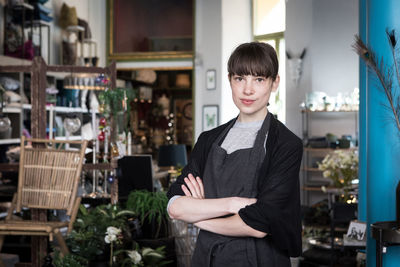 Portrait of confident young female entrepreneur standing with arms crossed at store