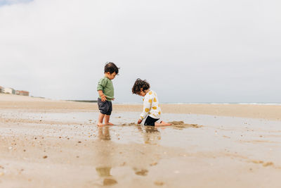 Rear view of friends enjoying on beach against sky