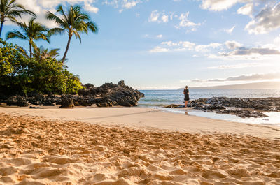 Rear view of woman standing on beach against sky