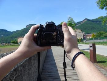 Cropped hands of man photographing against clear blue sky