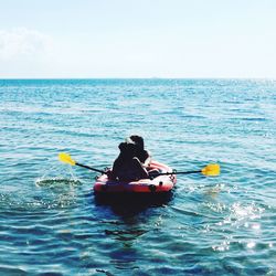 Rear view of people sailing on inflatable raft in sea against clear sky