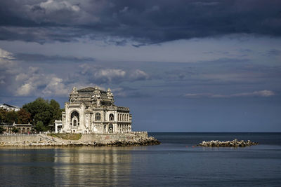 View of building by sea against cloudy sky