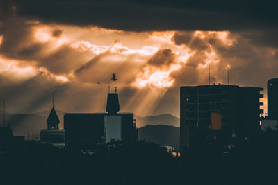 Silhouette buildings against cloudy sky during sunset
