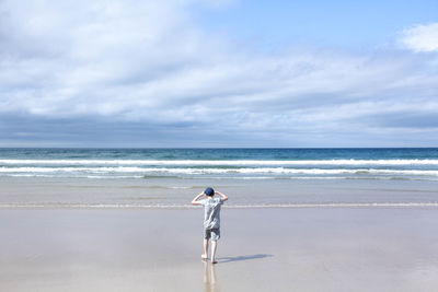 Rear view of man standing on beach against sky