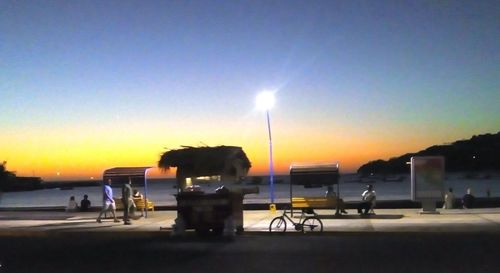 Silhouette people on illuminated street against sky at sunset