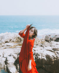 Portrait of woman holding her red dress while standing at beach during sunny day