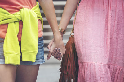 Midsection of friends holding hands while walking on street