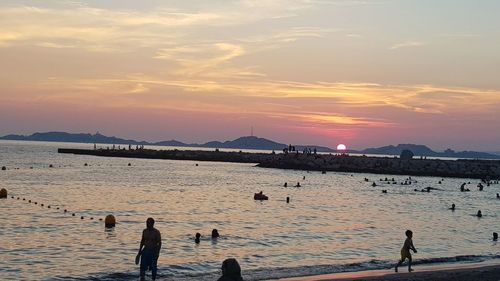 Silhouette people on beach against sky during sunset