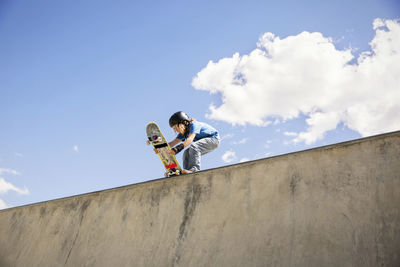 Low angle view of boy placing skateboard on ramp against blue sky