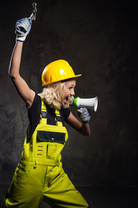 Female worker shouting on megaphone while standing against wall