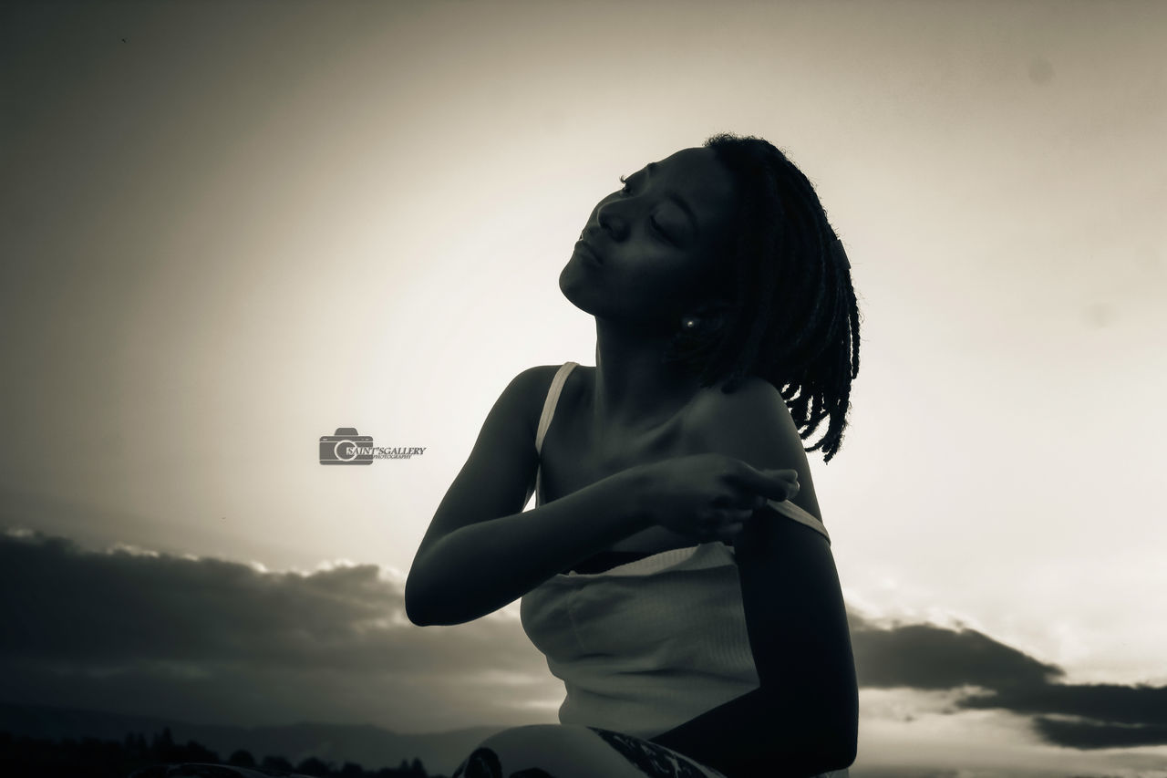 one person, sky, women, black, adult, darkness, silhouette, young adult, nature, white, black and white, monochrome, person, cloud, side view, lifestyles, female, backlighting, hairstyle, monochrome photography, sunset, sitting, outdoors, emotion, looking, light, copy space, waist up, back lit, hand, long hair, contemplation, standing