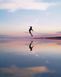 Silhouette woman jumping on shore against sky during sunset