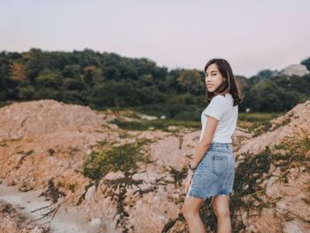 Portrait of smiling young woman standing on rock formation against clear sky during sunset