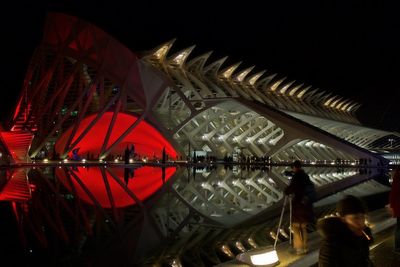 Reflection of illuminated building in city against sky at night