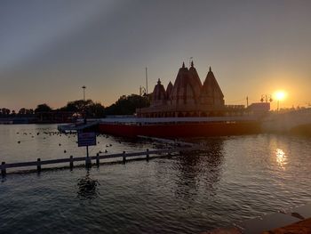 Scenic view of river by buildings against sky during sunset