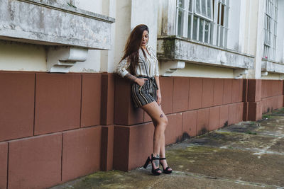 Full length portrait of woman standing against brick wall