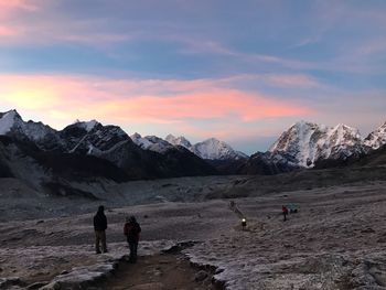 People walking on land against sky during sunset