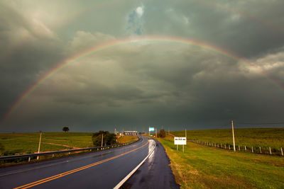 Rainbow over road against cloudy sky