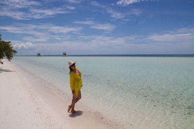 Full length of woman standing on shore against sky at beach during sunny day