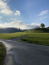 Empty road amidst field against sky