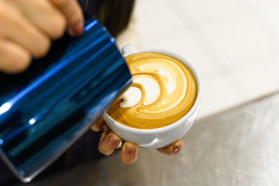 Hands of barista making latte or cappuccino coffee pouring milk, making latte art