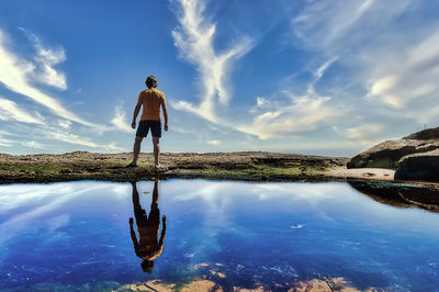 Rear view of man standing in lake against sky