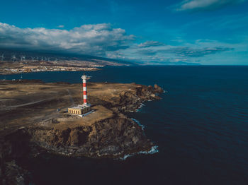 Lighthouse amidst sea and buildings against sky