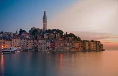 Buildings by sea against sky during sunset