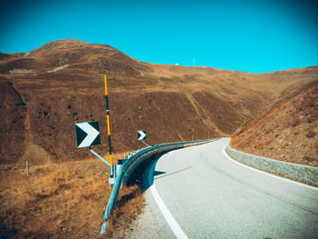 Road sign by mountain against clear blue sky