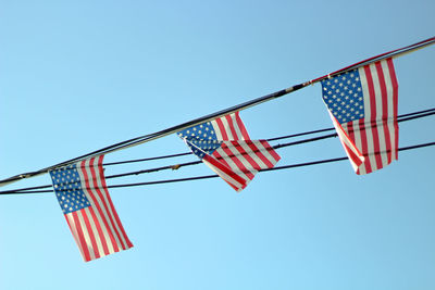 Low angle view of american flags hanging on cable against clear sky