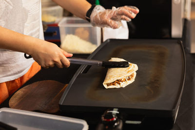 Woman preparing fresh quesadilla on black grill at local food market.