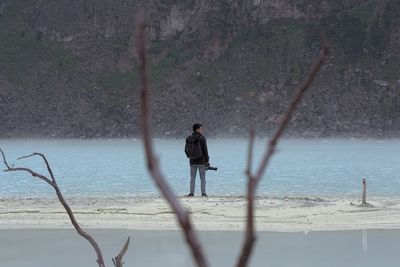 Rear view of man holding camera while standing at beach