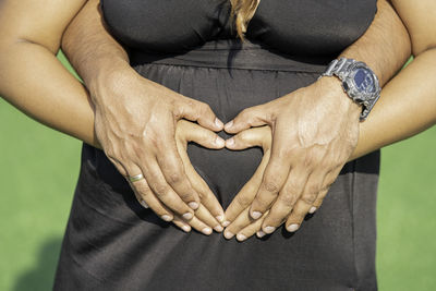Midsection of pregnant couple making heart shape over abdomen 