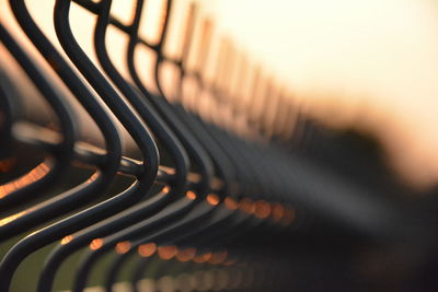 Close-up of metallic fence against sky during sunset