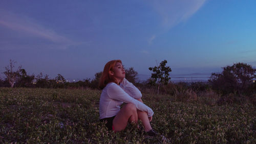 Woman sitting on field against sky