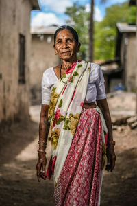 Portrait of senior woman in sari standing on road against houses