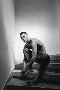 Side view of shirtless young man standing against wall