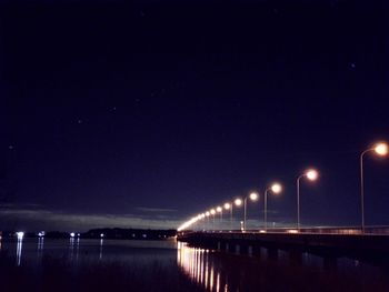 Illuminated bridge over river against sky at night