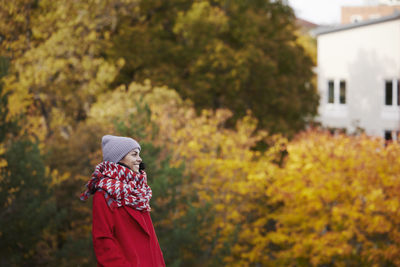 Side view of woman wearing hat standing against trees during autumn