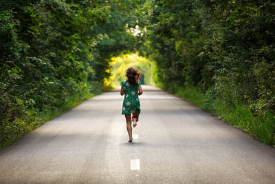 Rear view of woman running on road amidst trees