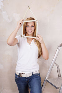 Portrait of young woman holding frame against wall