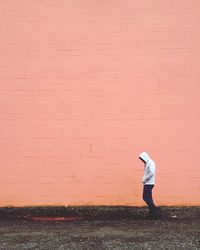 Side view of man in hooded jacket on sidewalk against pink wall