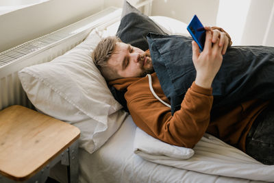 Lazy man using phone while lying on bed at home