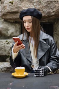 A happy european cyber woman with a bionic prosthesis on her arm is chatting in a smartphone